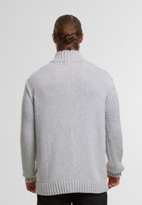 Jasnoszary sweter z dzianiny z wysokim kołnierzem, ściągaczami przy mankietach i dole. Posiada teksturowany geometryczny wzór i luźny krój.