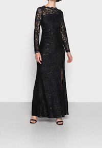 Černé krajkové šaty s dlouhými rukávy, se třpytkami, přiléhavým střihem, květinovým vzorem a rozparkem nad stehnem. Nosené s černými podpatky.