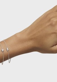 Bracciali in argento con charm a stella e luna su una mano, che mostrano una finitura metallica liscia e un design delicato sulla pelle.
