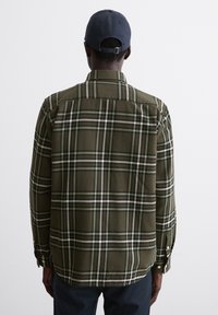 Camicia a quadri verde con strisce bianche e blu, polsini con bottoni e orlo curvo. Il tessuto appare morbido con una texture leggera. Vista posteriore.