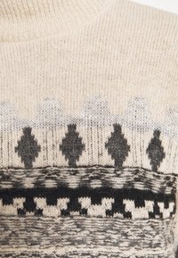 Pull en tricot beige avec des motifs géométriques et animaliers noirs et gris en bandes horizontales.