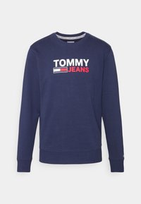 Mörkblå crewneck sweatshirt med långa ärmar, med vit och röd "TOMMY JEANS"-logotyp och flagg emblemet på bröstet.