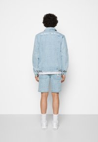 Light blue denim jacket and shorts set featuring intricate patterns, logo on the back, with a relaxed fit and visible hardware details.