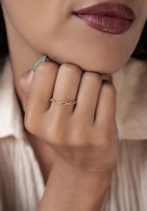Roségoldener, gewundener Bandring an einem Finger, kombiniert mit einem grün-blauen Akzentnagel. Teint ist warm, mit sichtbarer leichter Textur.