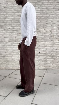 Long-sleeve white shirt paired with loose maroon sweatpants featuring elastic waist and side pockets, complemented by black shoes with textured accents.