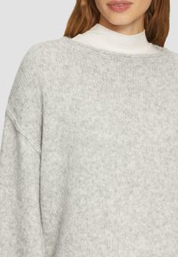 Jasnoszary, oversize sweter z dzianiny, wykonany z miękkiego materiału, z łódkowym dekoltem i opadającymi ramionami, zapewniający luźny krój.
