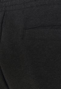 Pantalon de survêtement en coton noir avec une texture douce, une ceinture élastique et une poche arrière pour le rangement. Design simple et fonctionnel.