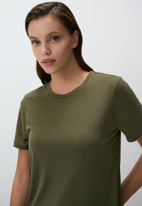 T-shirt in cotone verde oliva con scollatura rotonda e maniche corte, caratterizzato da una texture liscia e un design aderente senza adornamenti.