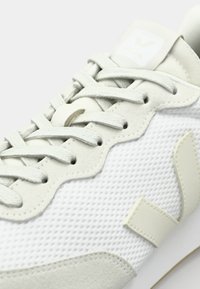 Hvite joggesko med mesh-overdel, semskede detaljer og snøring. Merkbar skjellformet design og logo på tungen. Lysegrå detaljer.