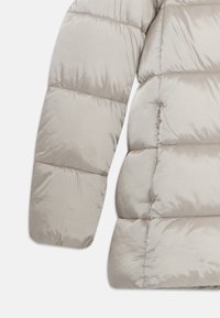 Lichtbeige gewatteerde pufferjack met een mouw en zijkant, zichtbaar ritszakje en horizontale stikdetails.