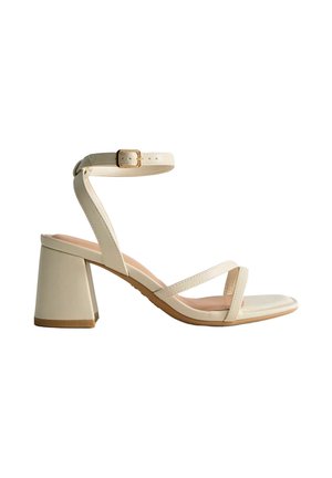 Sandale beige à bout ouvert avec bride à la cheville, talon bloc et deux fines lanières sur le pied, vue de profil sur fond blanc.