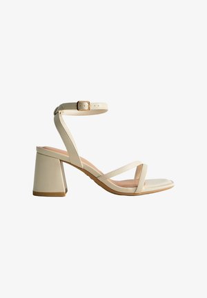 Sandale beige à bout ouvert avec bride à la cheville, talon bloc et deux fines lanières sur le pied, vue de profil sur fond blanc.