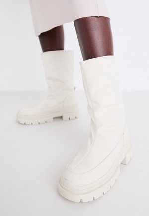 Botas blancas hasta el tobillo con un acabado suave y texturizado, que presentan una suela de goma gruesa y una forma esculpida para un diseño moderno.