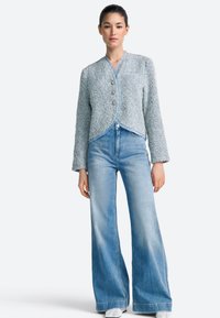 Svetlomodrá texturovaná bunda s okrúhlym golierom, prednými gombíkmi a dlhými rukávmi, v kombinácii s džínami s vysokým pásom a širokými nohavicami.