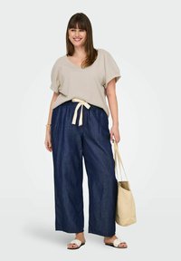 Beige ribbet V-hals top med korte ærmer, parret med mørkeblå vide bukser med et cremefarvet bånd og hvide sandaler. Inkluderer en beige taske.