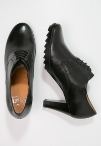 Chaussures en cuir noir avec un bout arrondi, un système de laçage, et un talon texturé, avec une finition lisse et de subtils détails de couture.