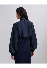 Vestido de satén navy con largas mangas abullonadas y un cuello alto; parte inferior texturizada con puntos en relieve; acabado de material suave.