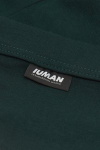Mörkgrön tyg med ribbad textur och en svart etikett med vit text "IUMAN" och "intimissimi uomo" sydd i kanten.