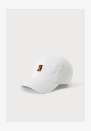 Casquette de baseball blanche avec un petit écusson du logo Nike en rouge, bleu marine et jaune sur le devant au centre, présentée sur un fond clair uni.