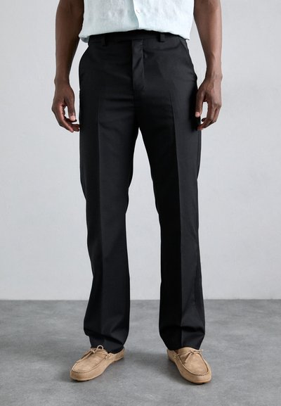 Black formal trousers with a straight cut, made from smooth fabric, featuring belt loops and a crease down the front. Worn with tan shoes.