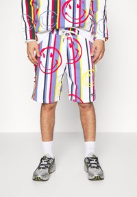 Multikleurige shorts met verticale strepen in rood, geel, blauw en zwart, versierd met grote smileyface-print en een elastische tailleband.