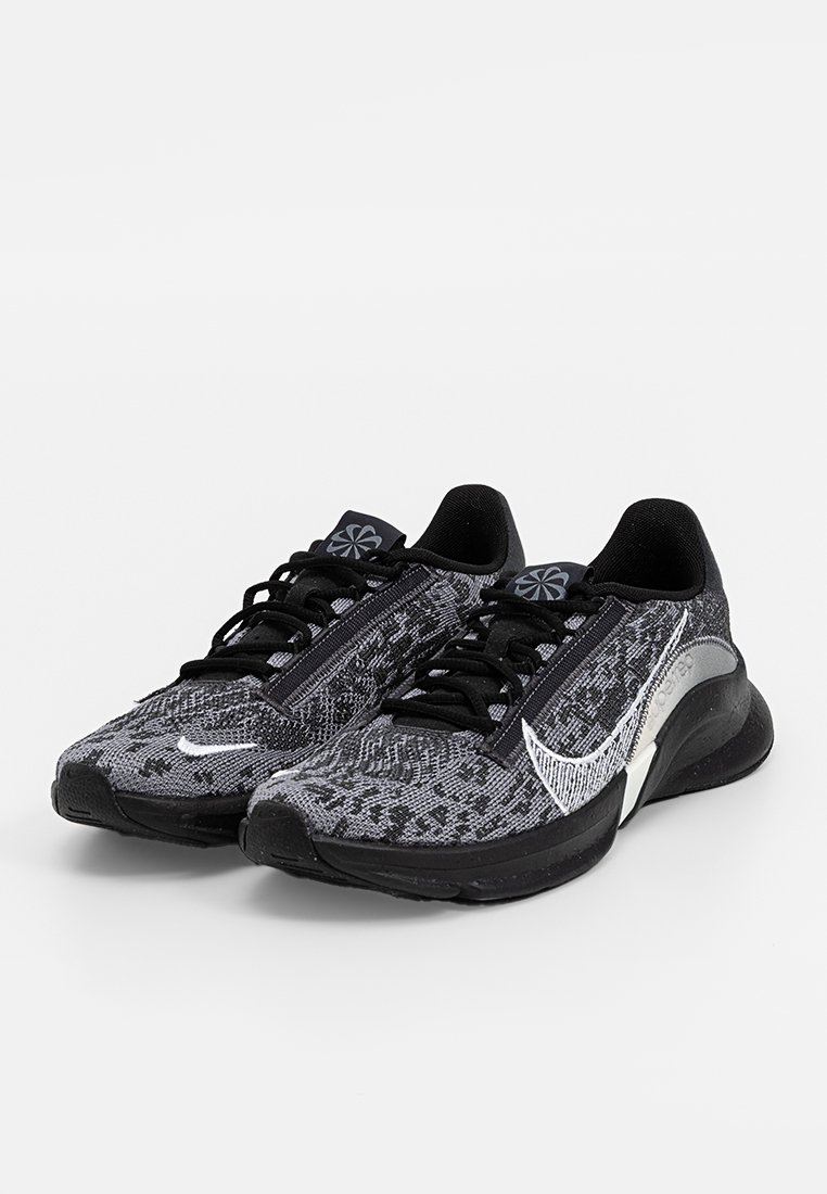 Zapatillas deportivas negras y grises con un upper texturizado, un destacado swoosh blanco de Nike y cordones negros; diseñadas para la comodidad y el rendimiento.