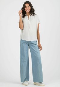 White short-sleeve blouse with a collar, paired with light blue wide-leg pants. Minimalist design, soft fabric, and casual fit. White sneakers.