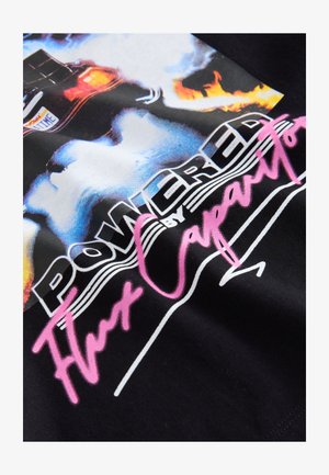 Maglietta nera con grafica colorata di un'auto con fiamme, testo "Powered by Flux Capacitor" in bianco e rosa. Tessuto di cotone morbido.