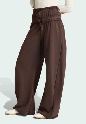 Pantaloni marroni scuri a gamba larga con vita alta arricciata e coulisse legata, indossati con scarpe bianche e un top leggero a maniche lunghe.