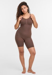 Body marrone con scollatura a barca e taglio simile a pantaloncini. Realizzato in materiale liscio e elasticizzato. Presenta bretelle regolabili e un design senza cuciture.