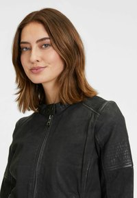 Schwarze Lederjacke mit hohem Kragen, Frontreißverschluss und gerippten Schulterakzenten. Glatte Textur und taillierte Passform.