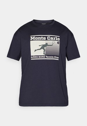 Laivansininen puuvillainen T-paita, jossa on grafiikkapainatus tennispelaajasta, teksti "Monte Carlo" sekä vaalean kerma- ja tumman vihreän värin vaakaraitoja.