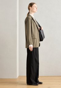 Blazer verde oliva con vestibilità rilassata, pantaloni neri a gamba larga e borsa nera. La texture è liscia con un design su misura.