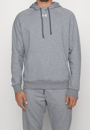 Mand iført en grå Under Armour hættetrøje med snørre og matchende grå joggingbukser mod en ensfarvet baggrund.