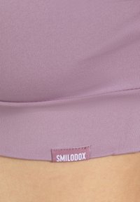 Lila sportliche Crop-Top aus glattem Material, mit passgenauer Schnittführung und einem kleinen, gestickten "SMILODOX"-Label nahe dem Saum.