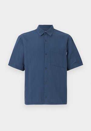 Chemise bleu marine à manches courtes, boutonnée, avec poche poitrine et col classique sur un fond uni.