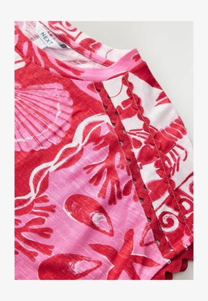 Camisa de estampado floral en rojo y rosa con bordes festoneados y patrones de conchas. Hecha de una tela ligera, presenta un escote redondo y mangas cortas.