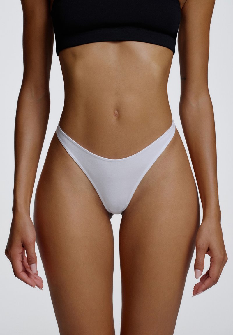 String blanc en tissu doux, avec une coupe taille basse et une couverture minimale, mettant en valeur une texture lisse et des lignes épurées.