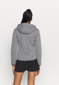 Giacca con cappuccio a fantasia in bianco e nero con design geometrico, maniche lunghe e silhouette aderente. Abbinata a pantaloni corti neri.