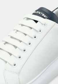Λευκό δερμάτινο αθλητικό παπούτσι με χοντρά λευκά κορδόνια και γλώσσα σε ναυτικό μπλε χρώμα με το λογότυπο της Valentino σε ασημί γράμματα.