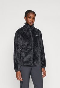 Zwarte fleece jas met een textuur, pluche oppervlak. Voorzien van een hoge kraag en een ritssluiting aan de voorkant. Logo weergegeven op de linkerborst.