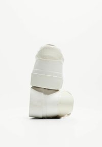 Baskets blanches avec un talon en cuir texturé, une semelle plateforme côtelée et un bout lisse. Design minimaliste sans marquage visible.