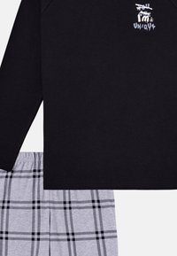 Black long-sleeve top with white graphic text, paired with gray plaid shorts featuring black and white lines. Soft cotton fabric.