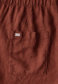 Shorts di lino color ruggine con vita arricciata e una singola tasca posteriore con un piccolo etichetta che recita "Street One Studio."