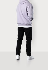 Felpa con cappuccio lilla dal taglio morbido e polsini a costine, abbinata a jeans neri e sneakers bianche. L'outfit presenta un look a strati.