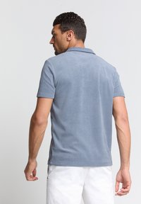 Lichtblauw polo shirt met een zachte textuur, korte mouwen en een kraag, voorzien van een zijsplit en contraststiksels.