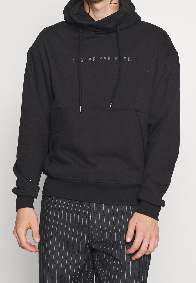 Schwarzer Kapuzenpullover mit Kordelzügen, ausgestattet mit einer Fronttasche und dezentem Branding. Hergestellt aus weichem Stoff mit einer lockeren Passform.