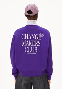 Paarse sweatshirt met grote witte tekst "CHANGE MAKERS CLUB" en een klein smiley-gezichtje detail op de bovenste rechterrug.