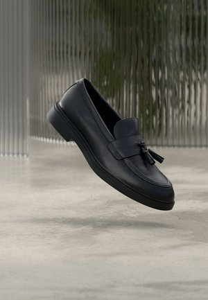 Czarne skórzane mokasyny o gładkiej fakturze, zaokrąglonym nosku i ozdobnych frędzlach z przodu. Elastyczna gumowa podeszwa z niskim obcasem.