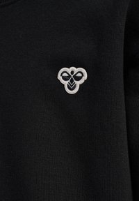 Svart stickad sweatshirt med en liten vit broderad bi-logotyp på övre vänstra bröstområdet. Tyget är slätt med ribbad textur.